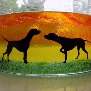 May include: A glass panel with a sunset scene featuring two black silhouettes of dogs facing each other. The glass panel has a textured surface and is framed in a silver metal frame.