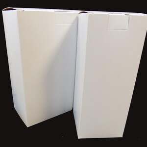 May include: Two white cardboard boxes, side by side, with the flaps closed. The boxes are rectangular and have a plain white surface.