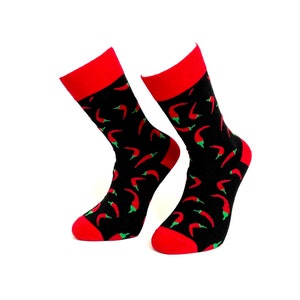 May include: A pair of black socks patterned with red chilli peppers and green stems. The socks feature red heels, toes, and cuffs. The socks are presented against a white backdrop.