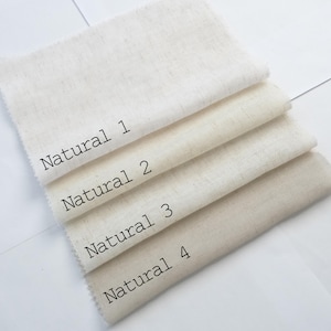 Pu&ograve; includere: Quattro campioni di tessuto rettangolari disposti in una pila, ognuno con una tonalit&agrave; distinta di bianco sporco o beige. I campioni sono etichettati con testo nero come Natural 1, Natural 2, Natural 3 e Natural 4, mostrando una trama tessuta.
