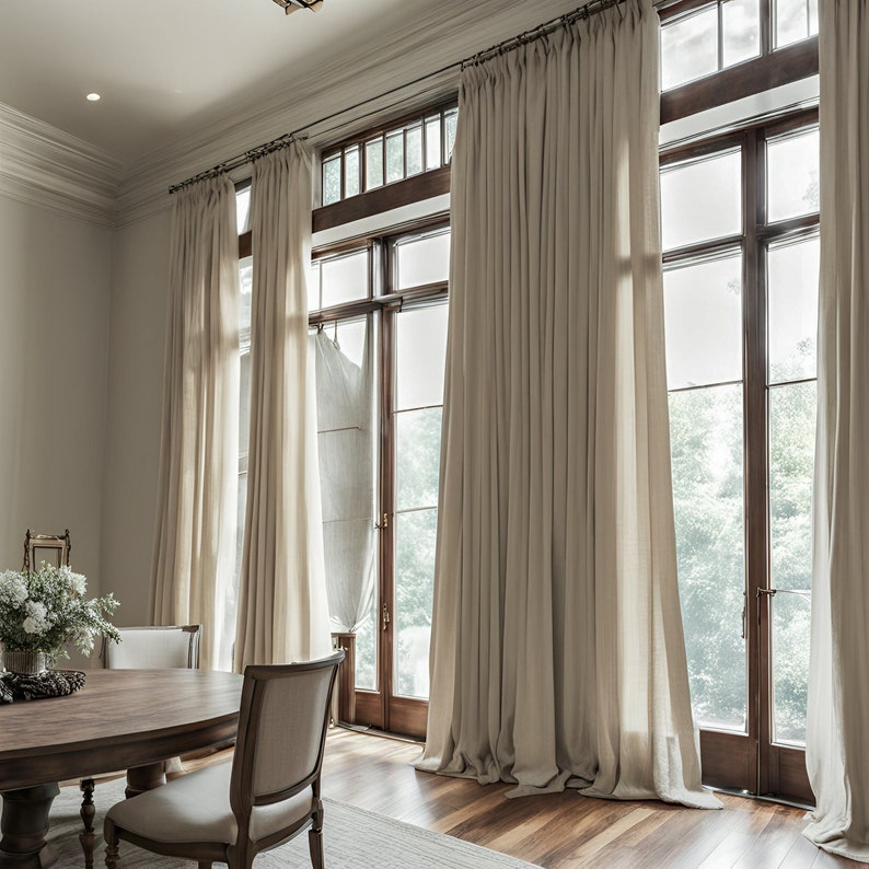 May include: A dining room with large windows featuring floor-length, cream-coloured linen curtains. The windows have wooden frames and offer a view of trees outside. A wooden table with chairs is in the foreground.