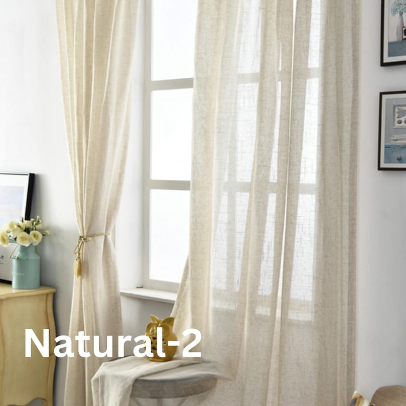 Pu&ograve; includere: Una coppia di tende lunghe fino al pavimento, semi-trasparenti, in tessuto beige chiaro simile al lino. Le tende pendono verticalmente, coprendo parzialmente una finestra, con un lato raccolto e legato con un cordoncino. Il testo Natural-2 &egrave; visibile.