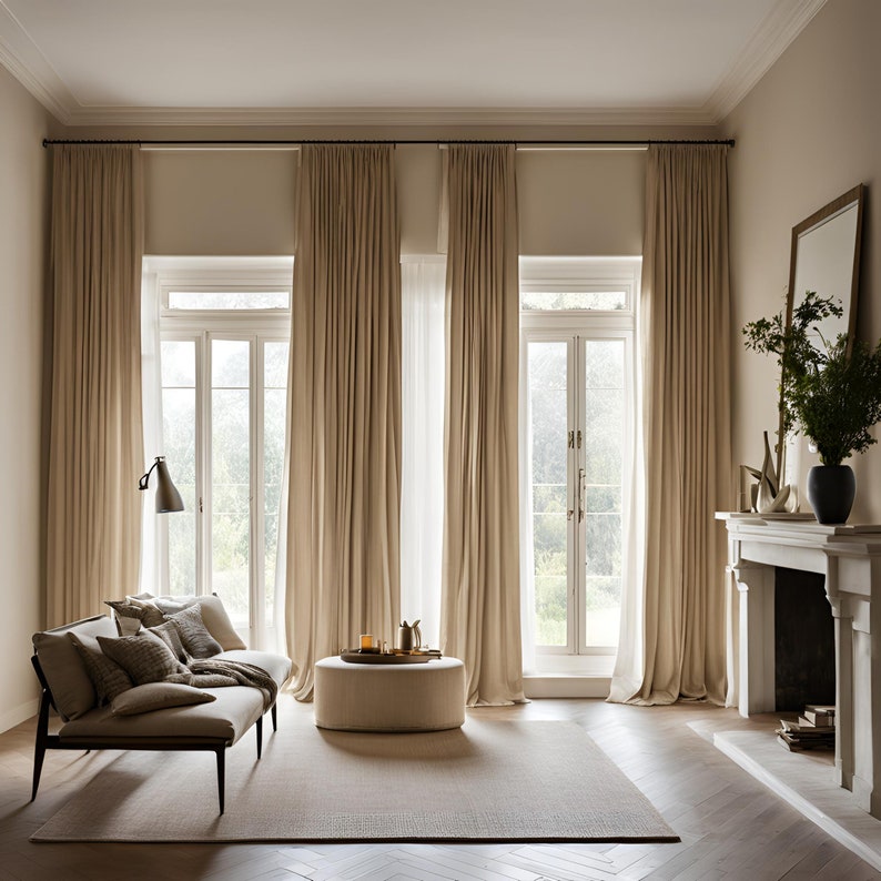 May include: Floor-to-ceiling beige curtains hang from a black rod over two white French doors. A beige sofa with matching throw pillows sits on a light rug next to a round beige ottoman. A fireplace with a mirror and a black vase is on the right.