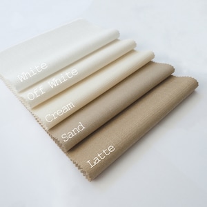 May include: Five rectangular fabric swatches arranged in a diagonal stack, featuring a woven texture. The colors are labeled with white text as White, Off White, Cream, Sand, and Latte, progressing from the lightest to the darkest shade.