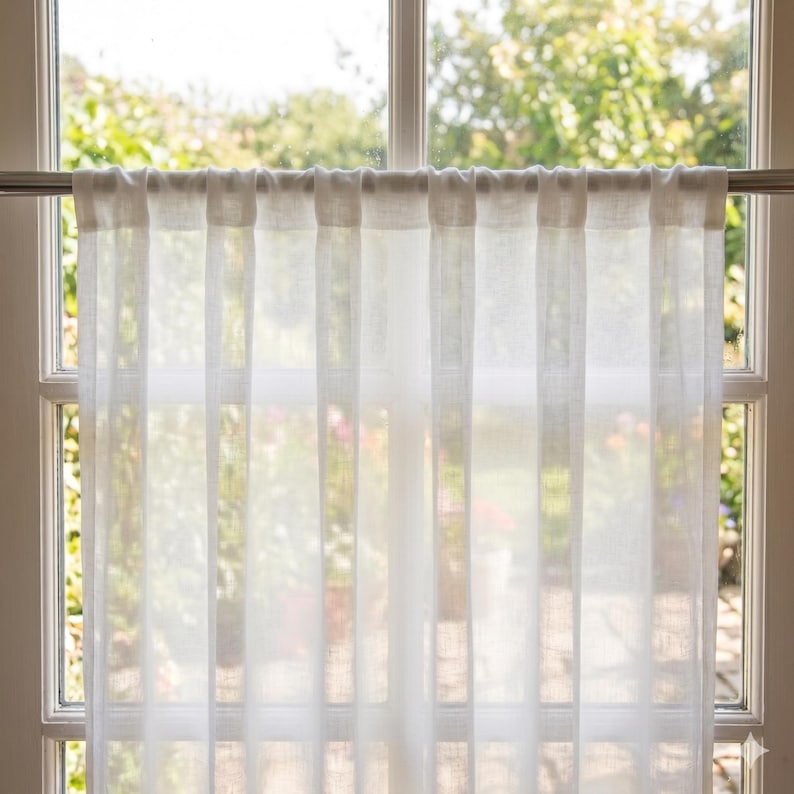 Pu&ograve; includere: Una tenda bianca semitrasparente con passanti, appesa a un bastone in metallo. Il tessuto presenta una trama visibile che lascia filtrare la luce, creando morbide pieghe verticali lungo tutta la superficie del vetro della finestra.