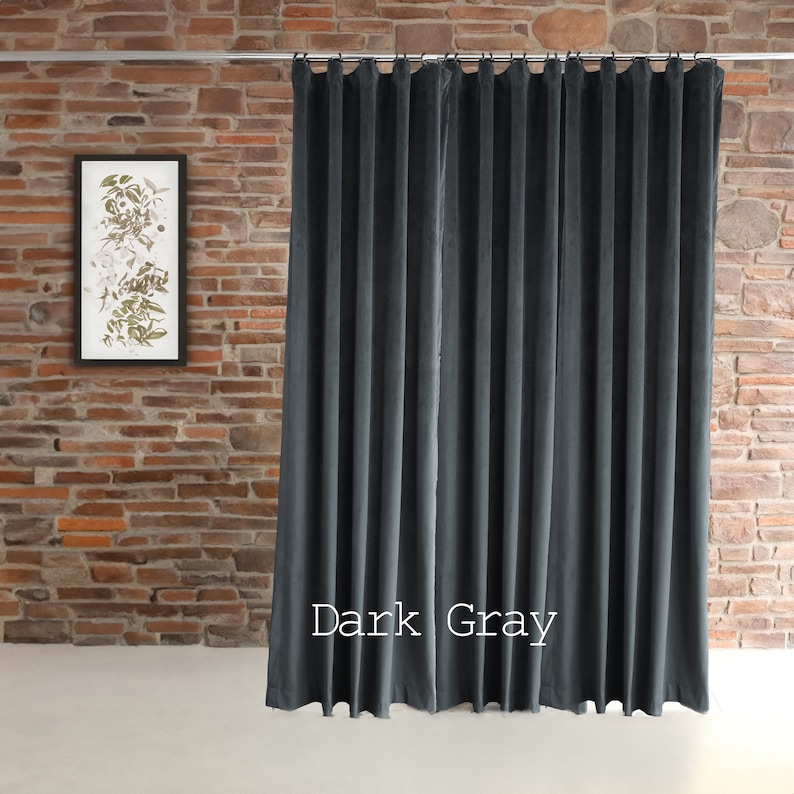 May include: Dark gray velvet curtain panel hanging from a metal rod. The curtain is pleated and has a soft, luxurious appearance. The text "Dark Gray" is displayed on the bottom right of the curtain. A framed botanical print hangs on a brick wall.