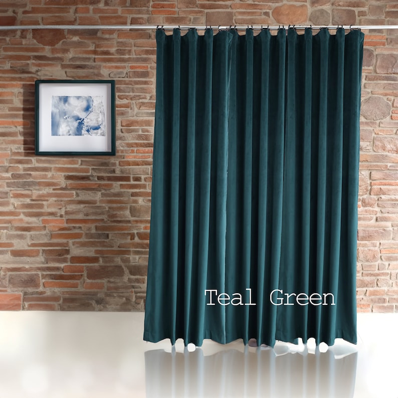 May include: Teal green velvet curtain hanging from a silver rod. The curtain is pleated and has a soft, luxurious appearance. The words "Teal Green" are printed on the curtain. A framed picture hangs on the brick wall.