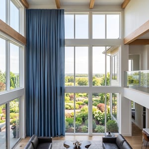 May include: Floor-to-ceiling blue curtains with vertical pleats covering a large window wall in a high-ceiling room. The curtains feature a uniform, dense fabric texture and hang straight from the top frame to the floor, framing a garden view.
