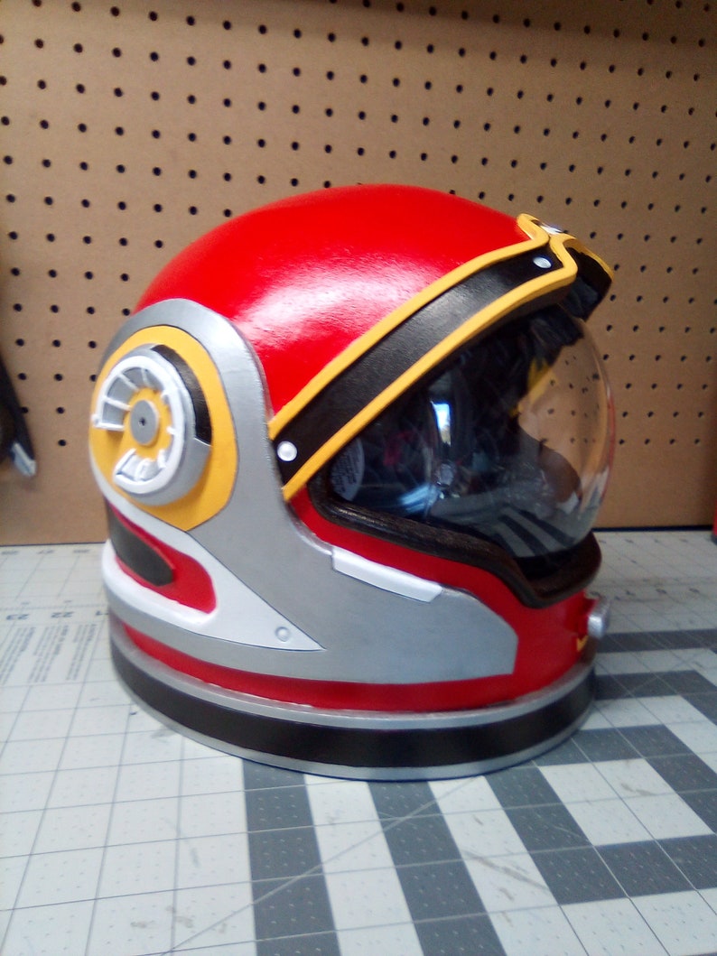 May include: A red, white, and black astronaut helmet with a yellow and black design on the side. The helmet has a clear visor and a black band around the top.