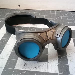 May include: A pair of silver steampunk goggles with blue lenses and a black adjustable strap.