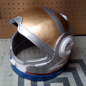 May include: A white, silver, and gold astronaut helmet with a blue and red stripe around the bottom.