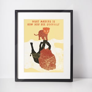 以下が含まれることがあります： 黄色い背景に、赤とオレンジの重ね合わせをした黒いライオンのシルエットが描かれた額装されたプリント。ライオンは背中に仰向けで、足を上げています。より小さいオレンジと黒のライオンの子のシルエットが、より大きなライオンの上に立っています。プリントの上部には黒い文字で「What matters is how you see yourself」と印刷されています。