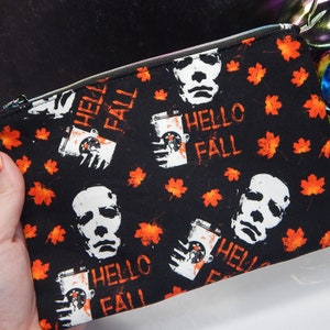 May include: Black zippered pouch with a repeating pattern of a white face mask, a coffee cup with the text "Hello Fall", and orange maple leaves.