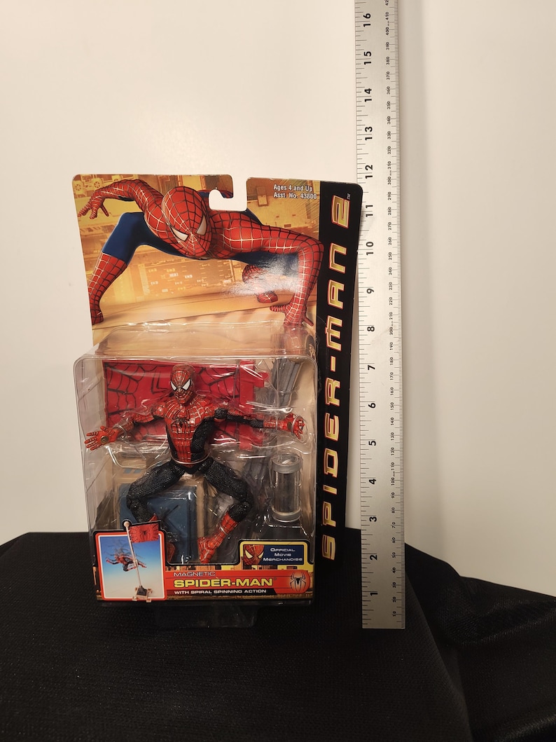 May include: Spider-Man 2 action figure in packaging. The figure is red and black, with blue accents. The packaging features Spider-Man in action poses. The figure is approximately 6 inches tall.