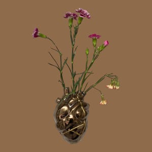 May include: A gold-colored, heart-shaped vase with a textured surface, holding several stems of pink and purple carnations. The vase has gold accents and is set against a brown background. A unique floral arrangement.