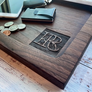 Pu&ograve; includere: Un vassoio in legno di noce scuro con una lettera "R" intagliata. Il vassoio rettangolare ha bordi rialzati. Monete, penne, un telefono e un portafoglio sono visibili sul vassoio. Il vassoio misura circa 30 cm di lunghezza.