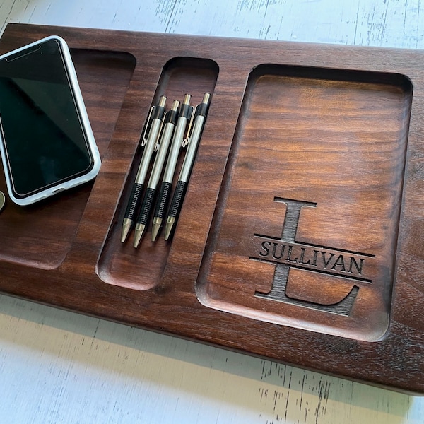Puede incluir: Una bandeja de madera marrón oscuro con cuatro compartimentos. La bandeja tiene una inscripción personalizada que dice "Sullivan" con una gran inicial "L". La bandeja es perfecta para organizar objetos pequeños como llaves, teléfonos y bolígrafos.