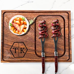 May include: A wooden serving board with a personalized monogram "TK" in the center. The board has two sections, one with a small white bowl filled with potato wedges and the other with two skewers of grilled meat.