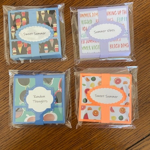 May include: Four small, square gift boxes wrapped in clear plastic. Each box has a different summer-themed design and a label with text. The boxes feature ice cream cones, fruit slices, and sunglasses. The labels read "Sweet Summer", "Summer Vibes", and "Random Thoughts".