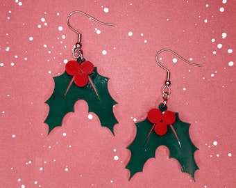 May include: A pair of green holly leaf earrings with red berries. The earrings have silver hooks.