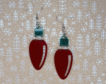 May include: A pair of red and green Christmas light bulb earrings. The earrings are made of metal and have a silver finish. The light bulbs are red and have a green top. The earrings are hanging from a silver hook.
