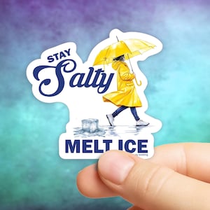 May include: A die-cut sticker with the words "Stay Salty" in a navy blue script. The sticker features a person in a yellow raincoat and umbrella, walking past a melting ice cube. The phrase "Melt Ice" is printed below.