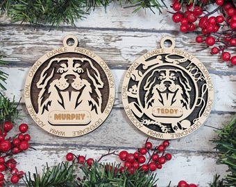 Può includere: Due ornamenti circolari in legno con ritratti di cani tagliati al laser. L'ornamento a sinistra mostra il nome MURPHY, mentre quello a destra presenta il nome TEDDY, la parola WOOF e piccole icone di un osso, collare, palla e zampa.