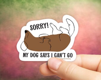 May include: A white sticker with a brown dog illustration lying on its back. The text "SORRY! MY DOG SAYS I CAN'T GO" is printed in black. The sticker is held by a hand against a blurred background.