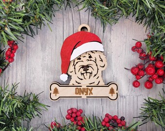 May include: A wooden Christmas ornament shaped like a dog head wearing a red and white Santa hat, positioned above a bone-shaped name tag engraved with the name ONYX and two small pine tree icons, featuring a hole at the top for hanging.