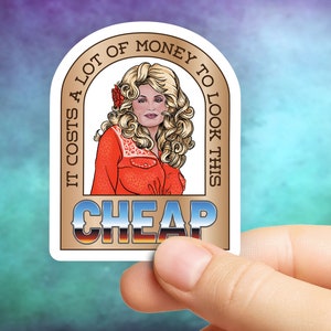 May include: A sticker featuring a cartoon illustration of a woman with blonde hair and a red outfit. The sticker has text that reads "IT COSTS A LOT OF MONEY TO LOOK THIS CHEAP."