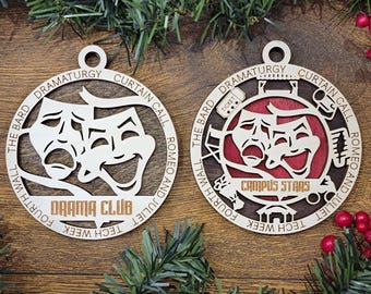 May include: Two circular wooden ornaments featuring theater masks. The left ornament says DRAMA CLUB. The right ornament has a red background, says CAMPUS STARS, and includes icons of a ticket, chair, and stage. Both feature text around the border.