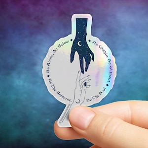 May include: Holographic sticker with a celestial design. It features two hands reaching towards each other, one filled with stars and a crescent moon. The sticker has the text "As Above, So Below" and "As Within, So Without". The sticker is held by a person's fingers.