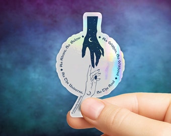 May include: Holographic sticker with a celestial design. It features two hands reaching towards each other, one filled with stars and a crescent moon. The sticker has the text "As Above, So Below" and "As Within, So Without". The sticker is held by a person's fingers.