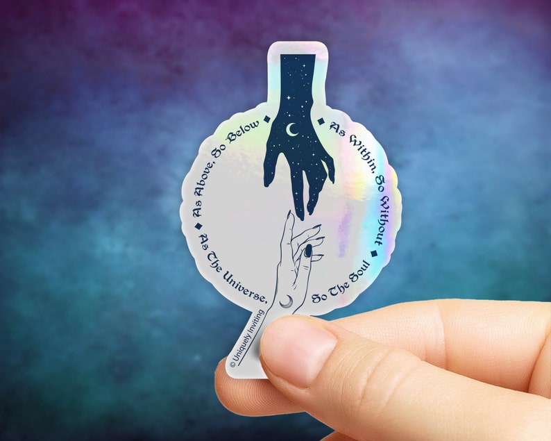May include: Holographic sticker with a celestial design. It features two hands reaching towards each other, one filled with stars and a crescent moon. The sticker has the text "As Above, So Below" and "As Within, So Without". The sticker is held by a person's fingers.
