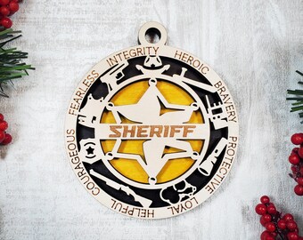 Könnte beinhalten: Ein kreisförmiges Holzornament mit einem zentralen gelben Stern, auf dem das Wort SHERIFF steht. Der äußere Rand enthält Ausschnitte von Polizeiausrüstung sowie die Wörter FEARLESS, INTEGRITY, HEROIC, BRAVERY, PROTECTIVE, LOYAL, HELPFUL, COURAGEOUS.