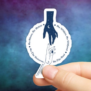 May include: A white sticker with a celestial design featuring two hands reaching towards each other. The top hand is filled with stars and a crescent moon. Text around the design reads "As Above, So Below" and "As Within, So Without."