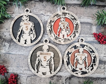 May include: Four circular wooden ornaments featuring American football player silhouettes. Two display the name MOLLY and number 5, while two display DECLERCO and number 5. The outer rings are engraved with football terms like PUNT and BLITZ.