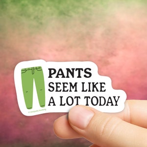 May include: A white sticker with a green pants graphic and the text "PANTS SEEM LIKE A LOT TODAY" in black. The sticker is held by a hand against a blurred background.
