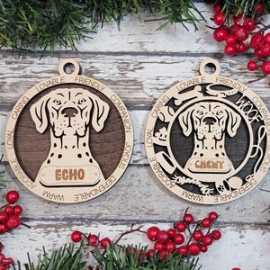 May include: Two circular wooden ornaments featuring a dog head cutout. The left ornament displays the name ECHO, while the right ornament features the name CHEWY and the word WOOF. Both include engraved words like LOVABLE, FRIENDLY, and LOYAL.