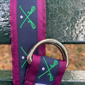 May include: A purple and navy blue dog collar with a green lacrosse stick design and a white bug logo tag.
