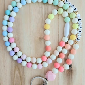 Puede incluir: Un cord&oacute;n de cuentas de colores con un dije de silicona rosa y un llavero plateado. Las cuentas son de tonos pastel de rosa, azul, verde y amarillo. El cord&oacute;n tiene una etiqueta de nombre con las letras "Miss Jessica" en negro.