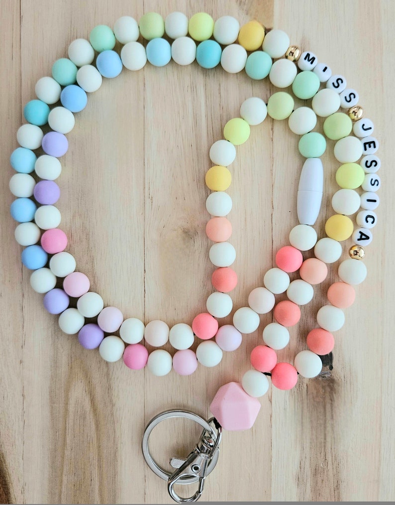 Puede incluir: Un cord&oacute;n de cuentas de colores con un dije de silicona rosa y un llavero plateado. Las cuentas son de tonos pastel de rosa, azul, verde y amarillo. El cord&oacute;n tiene una etiqueta de nombre con las letras "Miss Jessica" en negro.