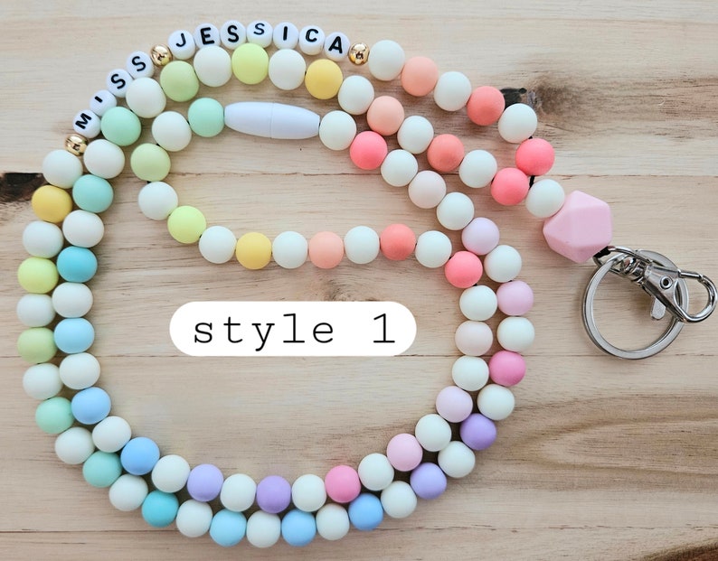 Puede incluir: Un cord&oacute;n de cuentas de colores pastel con un llavero plateado y las palabras "Miss Jessica" escritas en letras blancas. El cord&oacute;n est&aacute; hecho de dos hebras de cuentas, una en rosa pastel y la otra en amarillo y verde pastel.