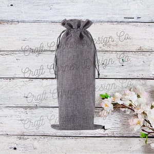May include: A gray burlap drawstring bag for holding a bottle of wine. The bag is sitting on a white wooden surface.
