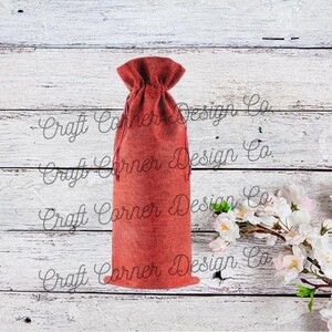 May include: A red burlap wine bottle bag with a drawstring closure. The bag is sitting on a white wooden surface.