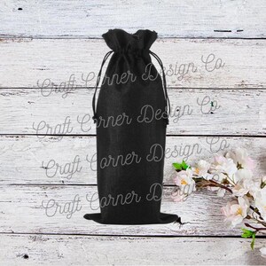 May include: Black burlap wine bottle bag with a drawstring closure. The bag is sitting on a white wooden surface.