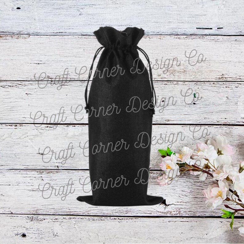 May include: Black burlap wine bottle bag with a drawstring closure. The bag is sitting on a white wooden surface.