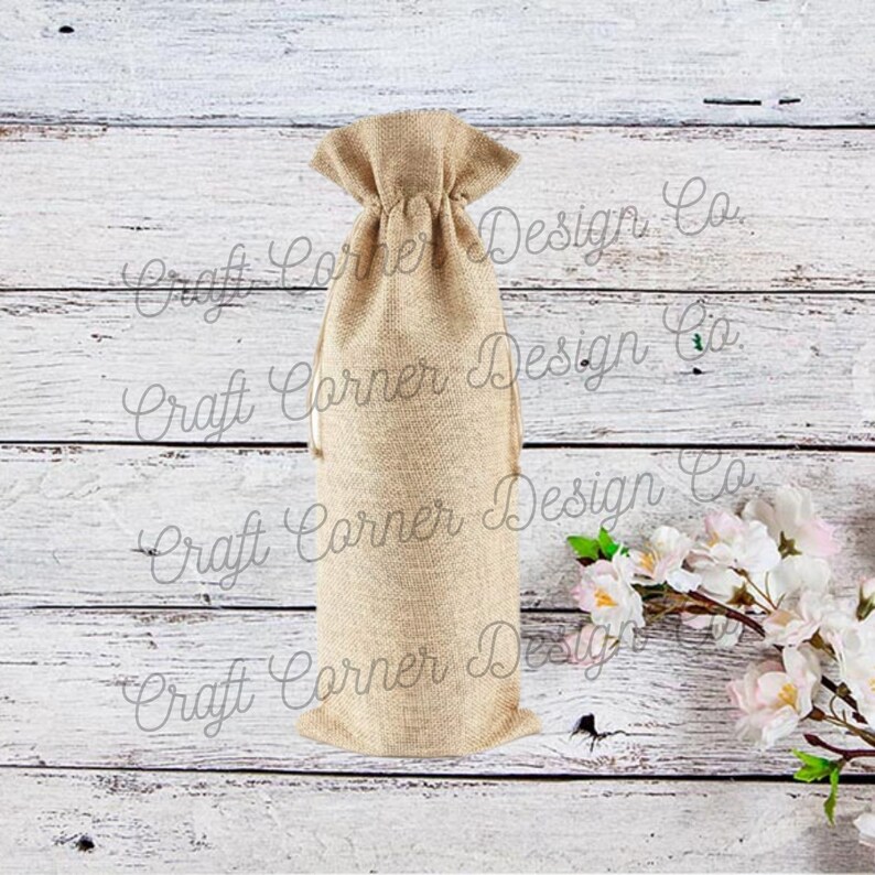 May include: A natural burlap wine bottle bag with a drawstring closure. The bag is sitting on a whitewashed wood background.