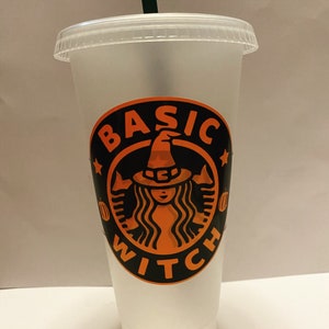 May include: A clear plastic reusable cold beverage cup with a lid and a green straw. The cup features a black and orange graphic with the words "BASIC WITCH" and a witch design, perfect for Halloween.