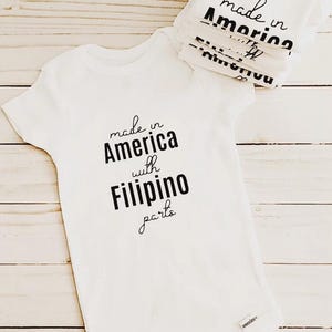 May include: White baby onesie with black text that reads "made in America with Filipino parts".